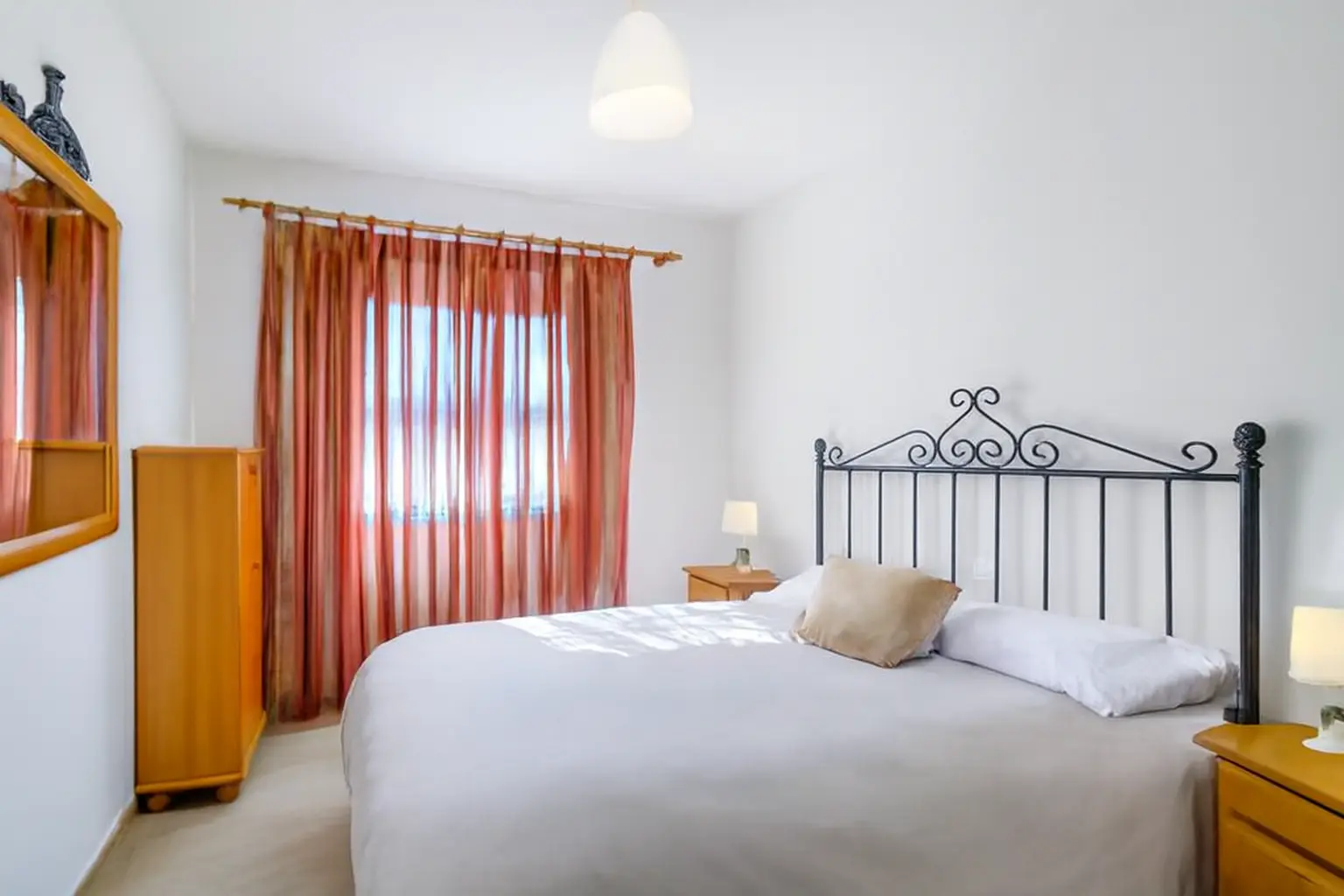 Schlafzimmer mit schmiedeeisernem Bett und orangen Vorhängen