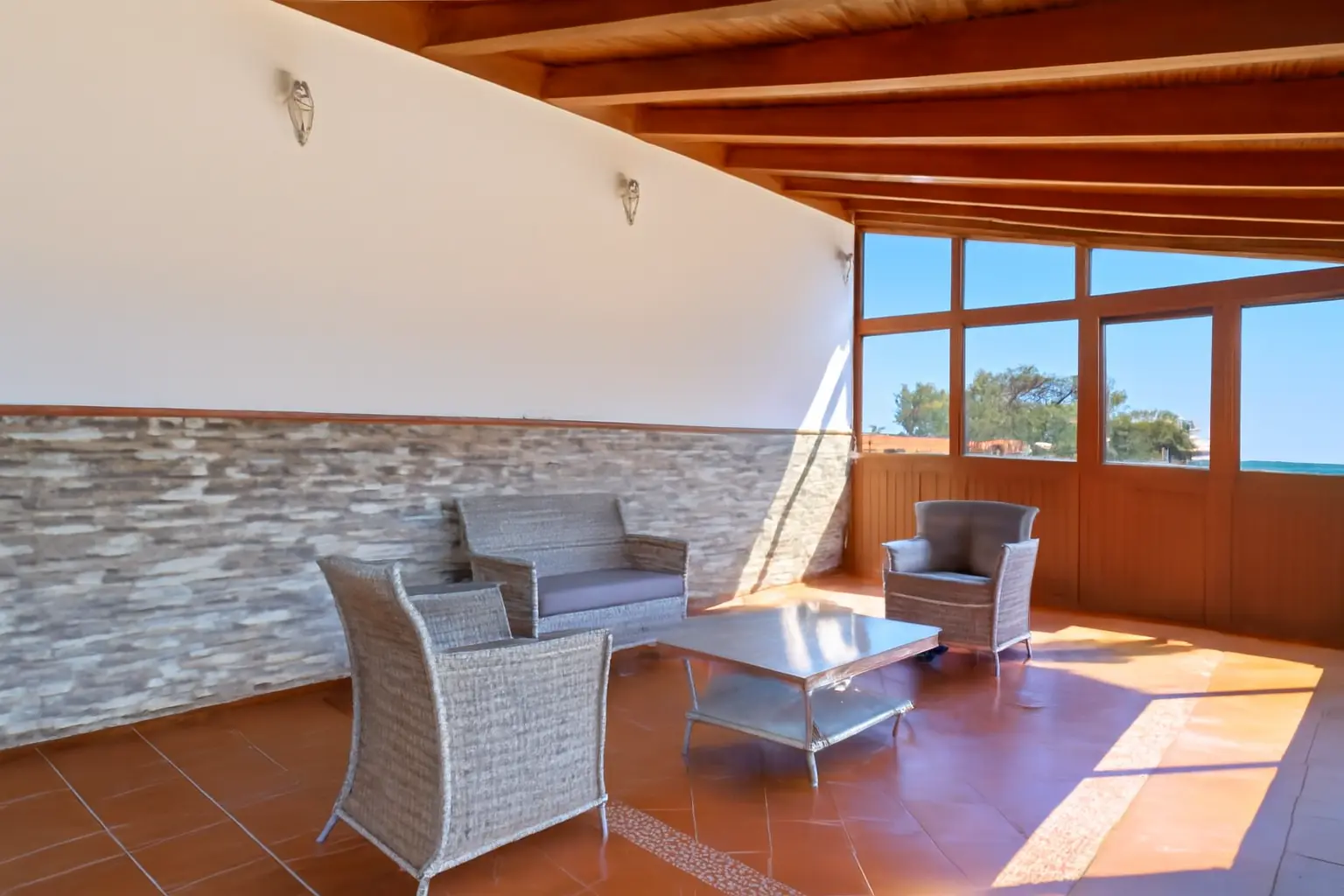 Überdachte Loungeterrasse mit Korbmöbeln und Natursteinwand